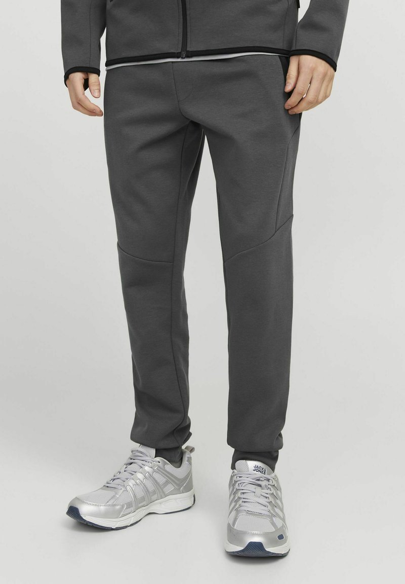 Gray athletic pants with a fitted design, featuring contrasting stitching, side pockets, and smooth texture. Paired with silver sneakers.