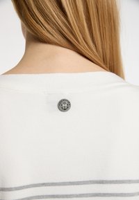 Maglietta bianca a maglia con righe orizzontali grigie, dotata di un bottone metallico rotondo con logo sulla parte posteriore del collo. Texture sottile e design casual.