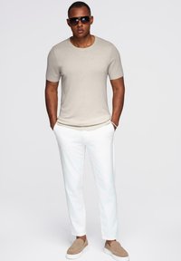 Béžová košile s krátkým rukávem, bílé tailored kalhoty a světle hnědé slip-on boty. Tmavé sluneční brýle dodávají outfitu elegantní akcent.