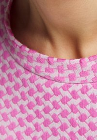 Top de manga corta en algodón rosa claro, con un patrón texturizado de formas entrelazadas en rosa más oscuro; escote redondo y acabado suave.