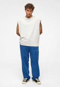 Lichtgrijs zonder mouwen top en blauwe velours broek. De outfit bevat zwarte sneakers met lichte accenten. Simpel en casual ontwerp.