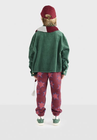 Žalias velveto oversize švarkas, bordo spalvos žvaigždžių rašo kelnės, žalia raštuota avalynė ir bordo spalvos kepurė. Detalė su kutu.