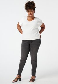 Witte kortermige top met een ronde hals, gecombineerd met donkergrijze slim-fit jeans en zwarte sandalen met blokhak en bandjes.
