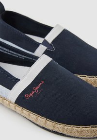 Bailarinas de lienzo en color navy con acentos blancos, suela de yute y logo rojo. Cuentan con paneles elásticos en los laterales para facilitar el uso y un diseño transpirable.