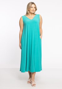 Ein türkisfarbenes, ärmelloses Maxikleid mit V-Ausschnitt aus weichem Stoff, das einen lockeren Schnitt und seitliche Taschen aufweist und eine fließende Silhouette hat.