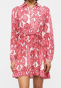 Robe chemise à manches longues, longueur genou, motif abstrait rouge et blanc, boutonnée à l'avant, col et ceinture nouée à la taille.