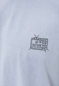 Camiseta de algodón azul claro con un dibujo en línea negra de una televisión vintage y el texto "SAL A FUERA" dentro de la pantalla.