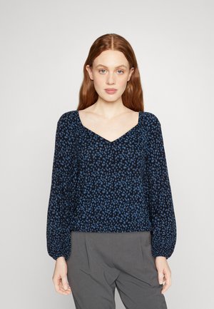 Blouse marine à motif floral bleu clair. Elle présente un décolleté carré et des manches longues élastiquées. Le matériau semble léger et texturé.