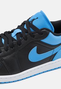 Baskets basses noires et bleues avec des lacets noirs, un swoosh Nike bleu clair et un logo Jumpman sur la languette bleue.