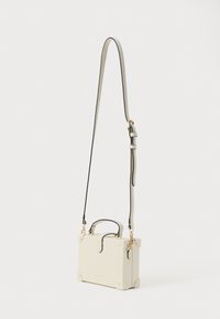 Cremefarvet rektangulær taske med top håndtag og lang justerbar skulderrem, guldfarvet hardware og hjørnebeskyttere på en hvid baggrund.