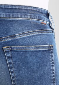 Blå denimjeans med en blekt finish, synliga sömmar, en bakficka och en liten brun läderetikett nära midjan.