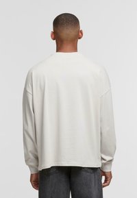 Top de manga larga color beige claro con un corte relajado, escote redondo y hombros caídos. Fabricado en un tejido suave con una textura lisa.