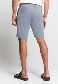 Grijze shorts van lichtgewicht materiaal, met achterzakken en een relaxed fit. Gekoppeld met zwarte sandalen.