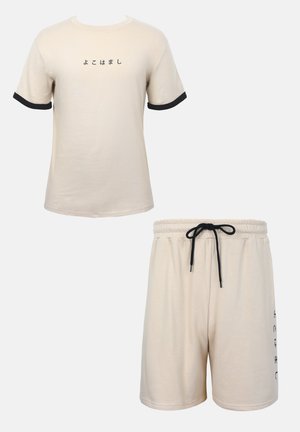 T-shirt beige à manches courtes avec bords de manches noirs et texte japonais, assorti à un short beige à cordon avec texte noir sur le côté.