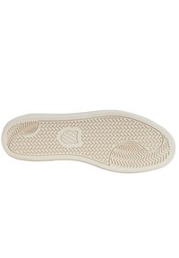 Suola di una scarpa, con una superficie beige chiaro tessurizzata che presenta un motivo a zigzag e un emblema circolare vicino al centro.