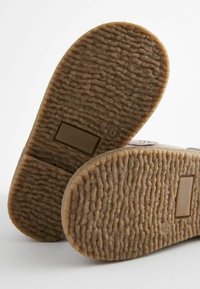 Suole di scarpe in gomma marrone con una superficie testurizzata e rigata. Presenta una piccola sezione rettangolare e un indicatore di taglia contrassegnato come "6".