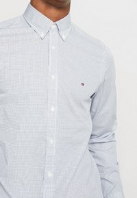 Jasnoniebieska koszula zapinana na guziki w kratkę, wykonana z bawełny. Posiada klasyczny kołnierzyk oraz małe, wyszywane logo na piersi.