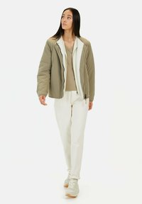 Hellgrüne gepolsterte Jacke mit weißem Sherpa-Futter, kombiniert mit einem beigen Oberteil und off-white Hosen sowie hellgrauen Sneakers.