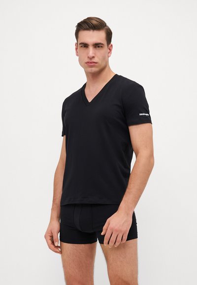 Schwarzes V-Ausschnitt-T-Shirt aus weichem Stoff mit kurzen Ärmeln, versehen mit einem kleinen weißen Logo auf dem linken Ärmel. Kombiniert mit schwarzen Boxer-Shorts.