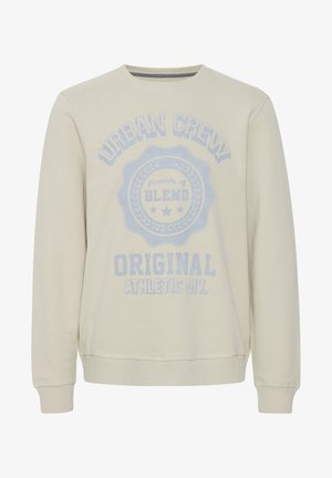 Heledad beežs pulover pikka käistega, ümar kaelus ja suur sinine graafiline tekst, mis sisaldab sõnumit "URBAN CREW" ja "BLEND" disainielemente.