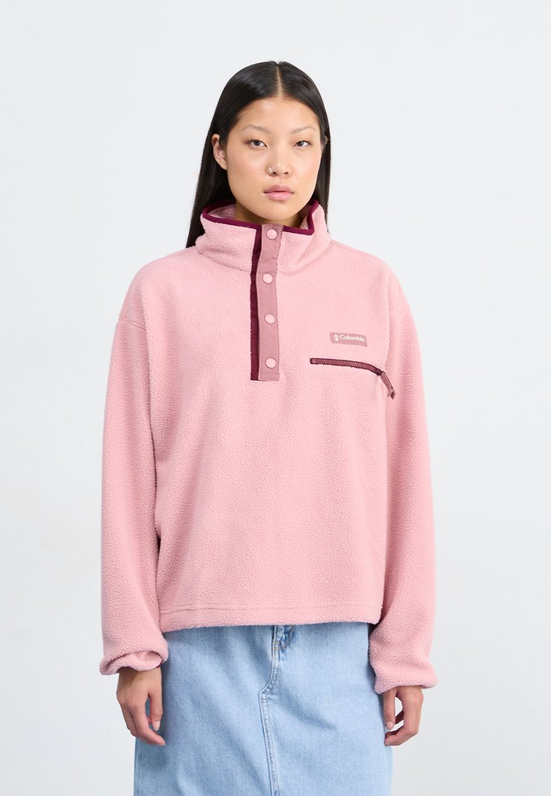 Pullover en polaire rose clair avec un col montant, deux boutons et une poche poitrine. Présente un accent bordeaux le long du col et de l'ouverture de la poche.