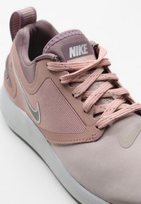 Sneakers Nike con tomaia in tessuto rosa chiaro, pannelli testurizzati, accenti argento e suola ammortizzata. Presentano una linguetta e lacci con il marchio.