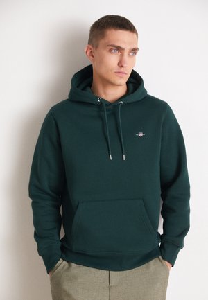 Dark green hoodie made from soft cotton, featuring a front pocket, drawstring hood, and a small logo in the chest area.