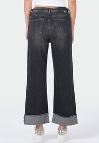 Brede-denim jeans in donkergrijs met rafelige uiteinden. Heeft twee achterzakken en een gladde textuur. Aansluitende taille met subtiele merkdetaillering.