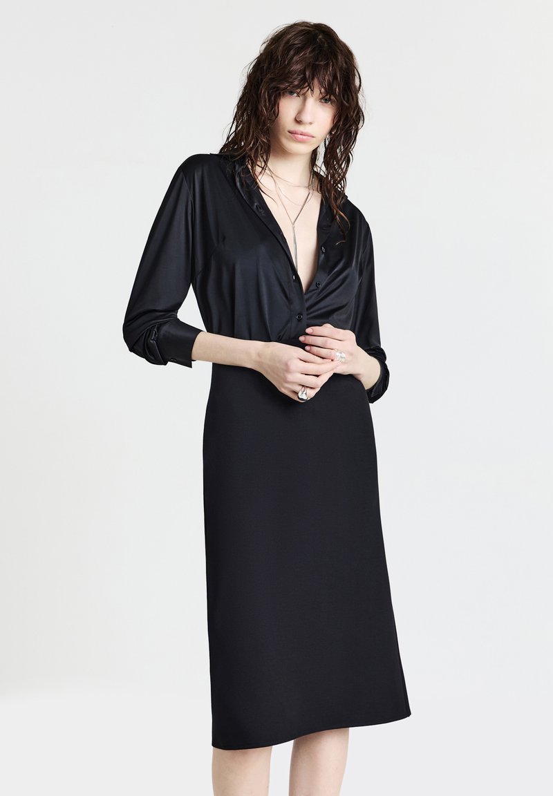 Schwarzes Knopfhemdkleid aus glattem Material, mit langen Ärmeln, einem V-Ausschnitt und einer geraden Silhouette, die bis zur Mitte der Waden reicht.