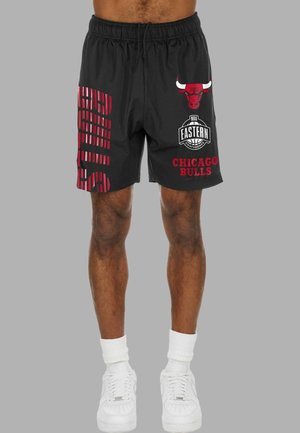 Schwarze Shorts mit dem Chicago Bulls-Logo, dem NBA Eastern Conference-Emblem und rotem vertikalem "Bulls"-Text, getragen von einer Person mit weißen Sneakers und Socken.