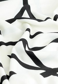 White fabric featuring large, bold black abstract patterns, smooth texture with slight sheen, draped with soft folds and creases.