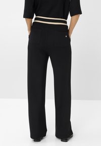 Schwarz breite Hosen mit einem gerippten, beigen und schwarzen elastischen Taillenbund. Verfügt über zwei Gesäßtaschen und eine glatte, weiche Textur.
