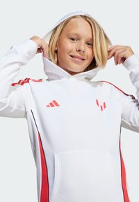 Haut à capuche blanc avec des accents rouges et des rayures noires sur les côtés. Présente une poche kangourou et une capuche ajustable. Logo Adidas sur la poitrine. Matériau doux.
