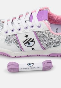 Baskets pailletées blanches et argentées avec bordure rose, logo œil violet et étoiles, lacets blancs, et lacets supplémentaires violets portant l’inscription Chiara Ferragni.