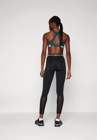 Reggiseno sportivo in verde scuro con accenti in rete e design racerback, abbinato a leggings neri con pannelli trasparenti e cintura con logo.