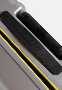 Contenitore di stoccaggio grigio con superficie liscia, dotato di una zip nera con accenti gialli e una maniglia testurizzata etichettata "Refugillean."
