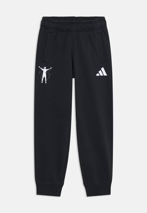 Black sweatpants feature a drawstring waist, side pockets, and white graphic designs, including a figure and the Adidas logo on one leg.