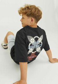 Svart t-shirt med kort ärm och grafisk design som har ett cirkulärt mönster samt texten "ART DISTRICT" i blått. Matchad med ljus denimshorts.