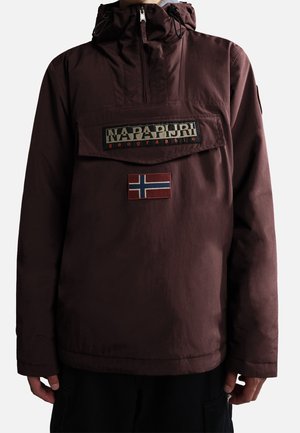 Personen bærer en mørk kirsebærrød hættejakke med en klaplomme foran, der viser "Napapijri geographic"-logoet og en lille norsk flagpatch nedenunder.