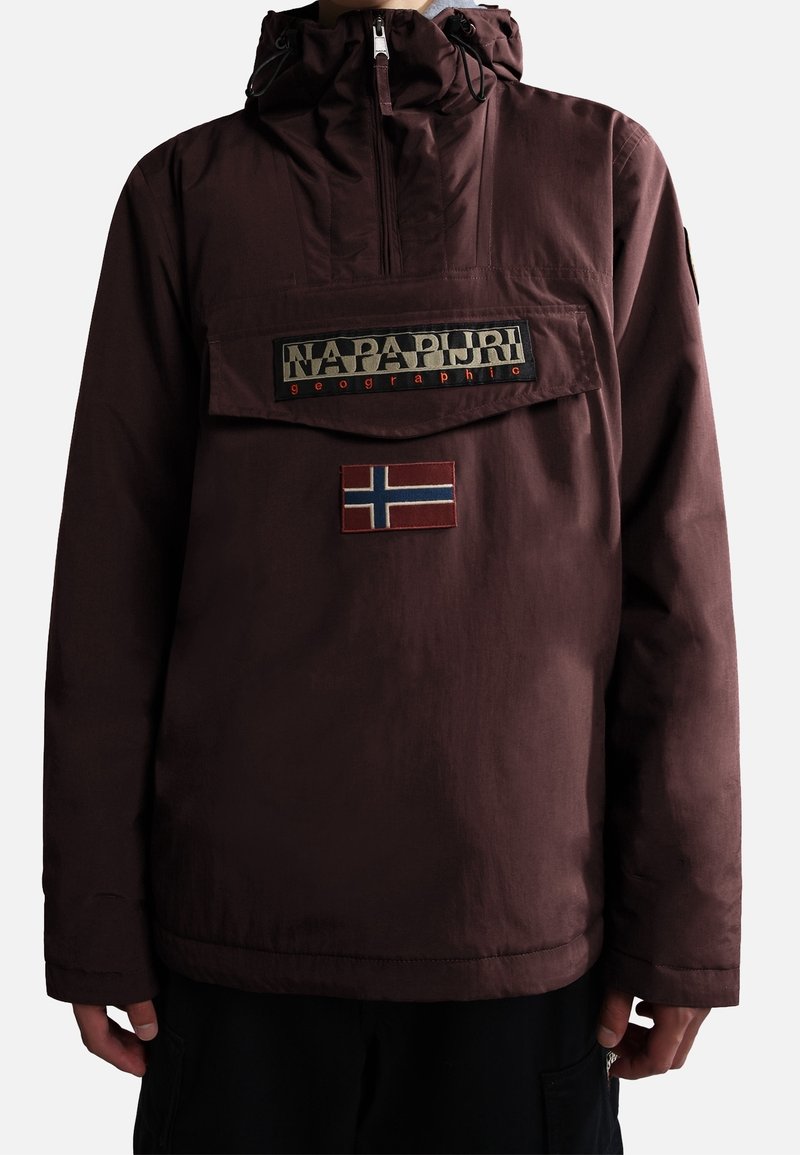 La personne porte une veste à capuche bordeaux foncé avec un rabat de poche avant affichant le logo "Napapijri geographic" et un petit écusson du drapeau norvégien en dessous.