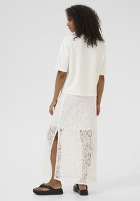 Haut blanc à manches courtes associé à une jupe maxi en dentelle avec des fentes latérales et des sandales à plateforme noires. Contraste entre la dentelle texturée et le tissu lisse.