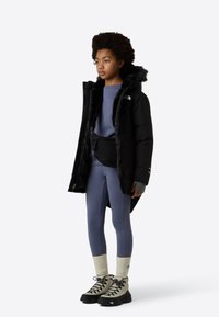 Μαύρο μπουφάν παφλασμού με κουκούλα επενδεδυμένη με γούνινη φόδρα, σε συνδυασμό με μπλε μπλούζα μακρυμάνικη, γκρι κολάν και εκρού κάλτσες με μαύρες και γκρι μπότες.