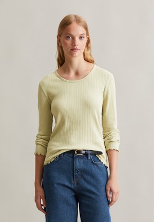 Haut à manches longues rayé jaune clair avec un col rond et un ourlet en dentelle, associé à un jean en denim bleu foncé et une ceinture noire.