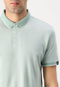 Lys grønn polo skjorte med teksturert stoff, med klassisk krage, tre-knaps placket og kontrasterende hvite detaljer på kragen og mansjettene.