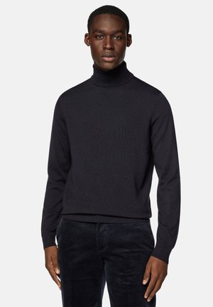 Dark navy turtleneck sweater in a ribbed texture, with long sleeves and a fitted silhouette, paired with dark corduroy pants.
