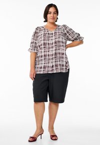 Blouse à manches courtes en soin de bourgogne et blanc avec des boutons, associée à un short bermuda noir. Le mannequin porte des talons rouges à brides.