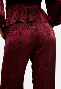 Bordové vzorované nohavice s hodvábnou textúrou, s komplikovanými čiernymi vzormi a elastickým pásom pre priliehavý vzhľad.