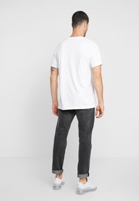 Wit katoenen T-shirt met een ontspannen pasvorm, gecombineerd met donkergrijze denim jeans. De schoenen zijn wit met transparante zolen en opgerolde boorden.