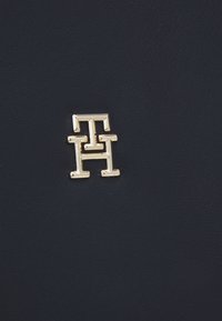 Materiale in pelle blu Navy con un emblema in tono oro che presenta lettere interconnesse "TH" in un design moderno e sobrio.