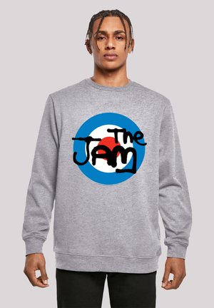 Gray sweatshirt with long sleeves, featuring a circular design in blue, white, and red, with the word "The Jam" in bold black text.